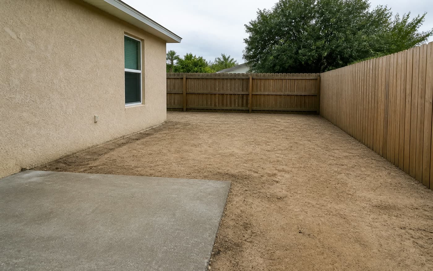 Unused sandy side yard beside a Florida home with bare soil and an open concrete patio