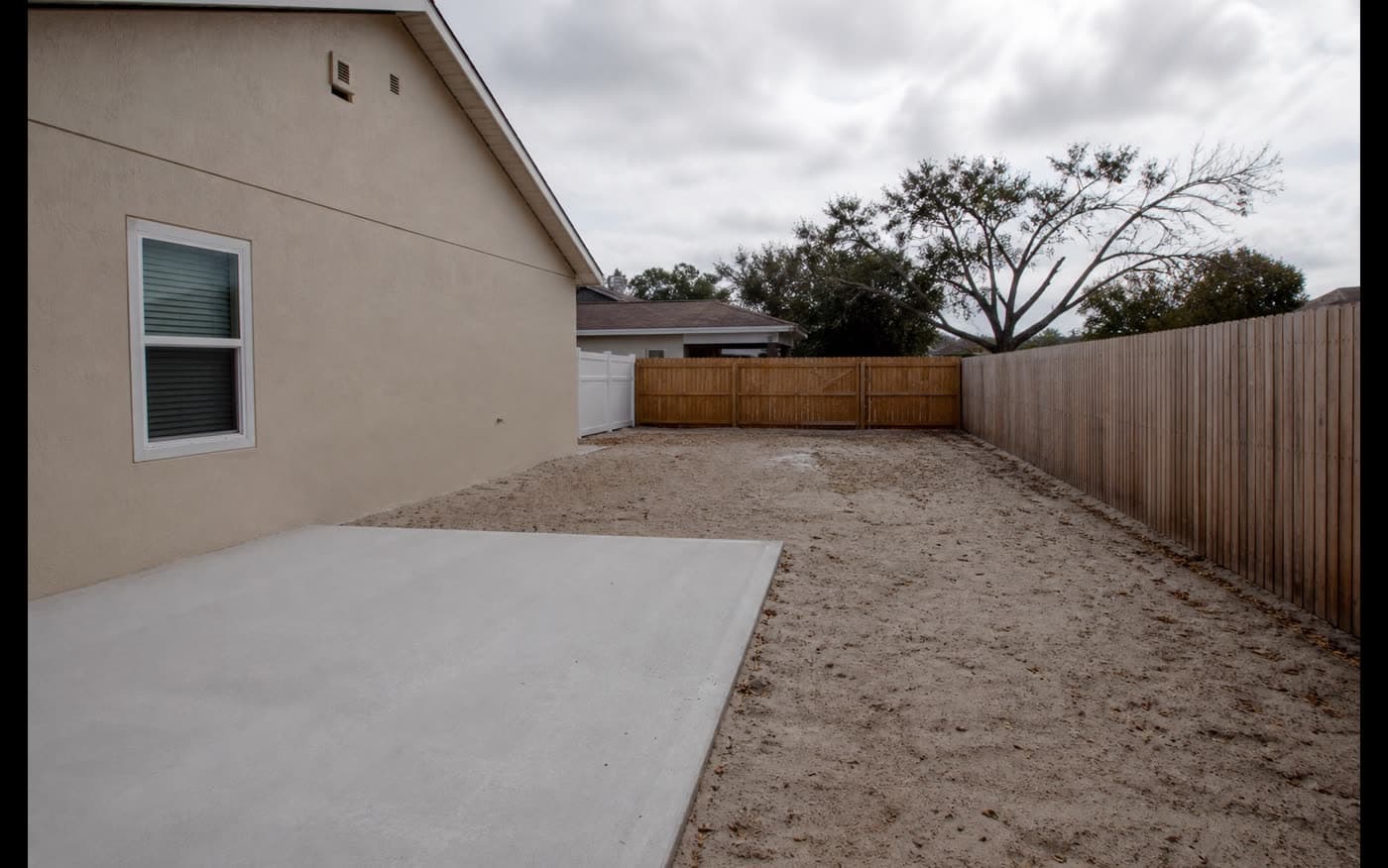 Unused sandy side yard beside a Florida home with open concrete patio before edible garden installation
